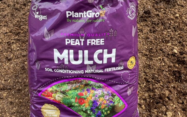 PlantGrow peat-free mulch 50 litre bag on soil, purple packaging with flower imagery and vegan certification