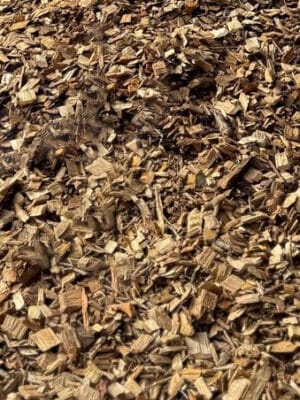 A close-up of Woodchip shows a large pile of small, rough, brown pieces of wood and bark scattered across the ground.