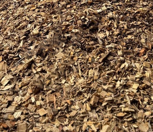 A close-up of Woodchip shows a large pile of small, rough, brown pieces of wood and bark scattered across the ground.