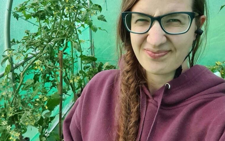 Woman in glasses beside growing tomato plants in greenhouse, promoting peat-free gardening practices.