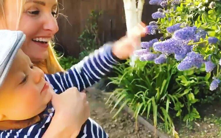 Child tending purple flowers in a garden flower bed with green foliage and soil.