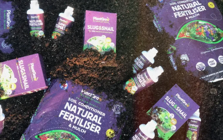 PlantGrow organic gardening products displayed on soil: natural fertiliser bottles, slug snail deterrent packets, and soil conditioner with mulch packaging.