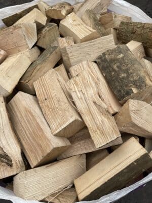 Kiln Dried Hardwood Firewood logs with rough, pale surfaces and some bark are stacked closely together in a large container.