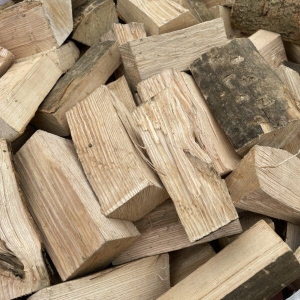 Kiln Dried Hardwood Firewood logs with rough, pale surfaces and some bark are stacked closely together in a large container.