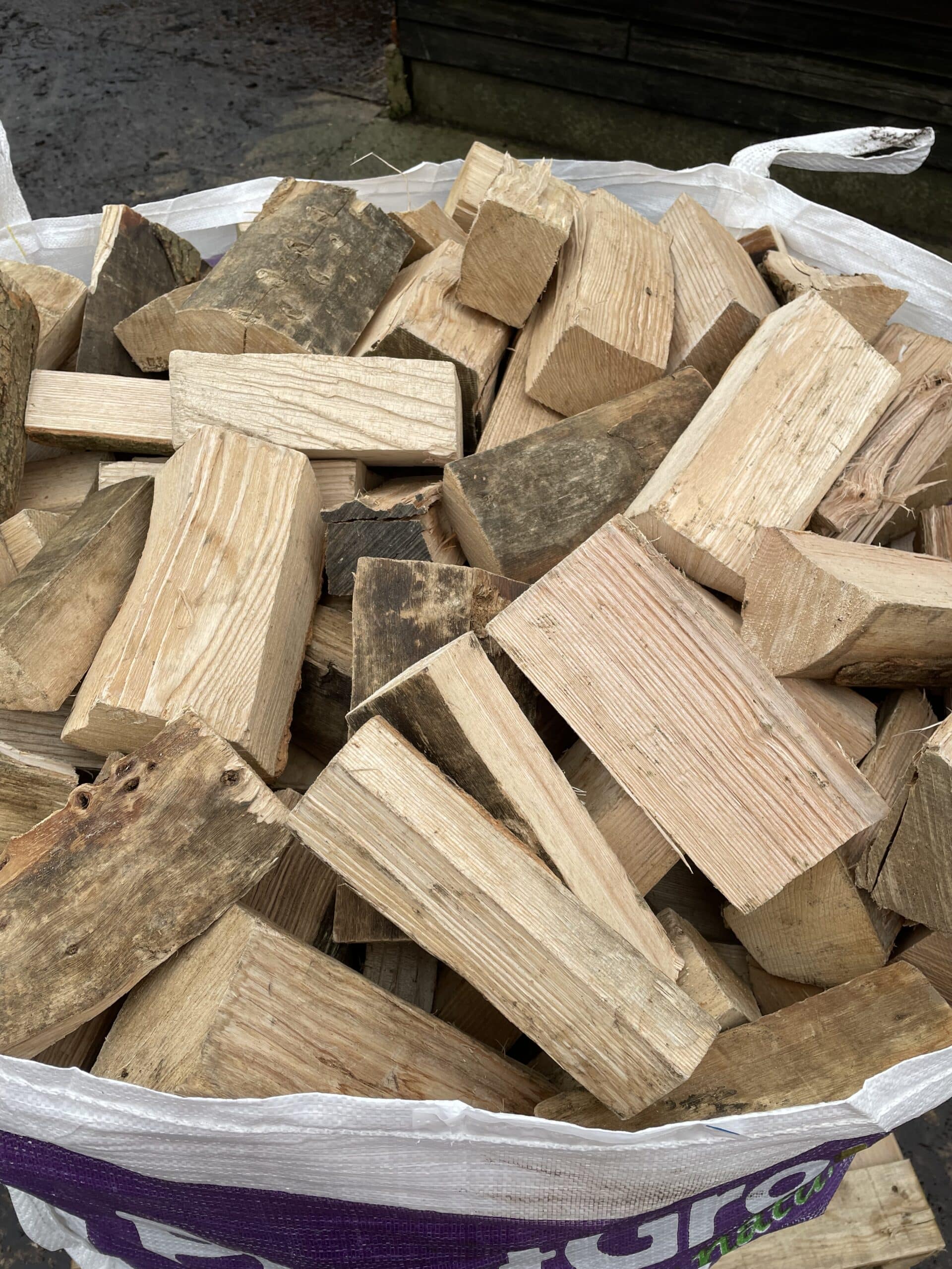 Bulk bag of kiln dried hardwood firewood logs, cut to 9 inches, showing mixed ash and beech pieces ready for use.