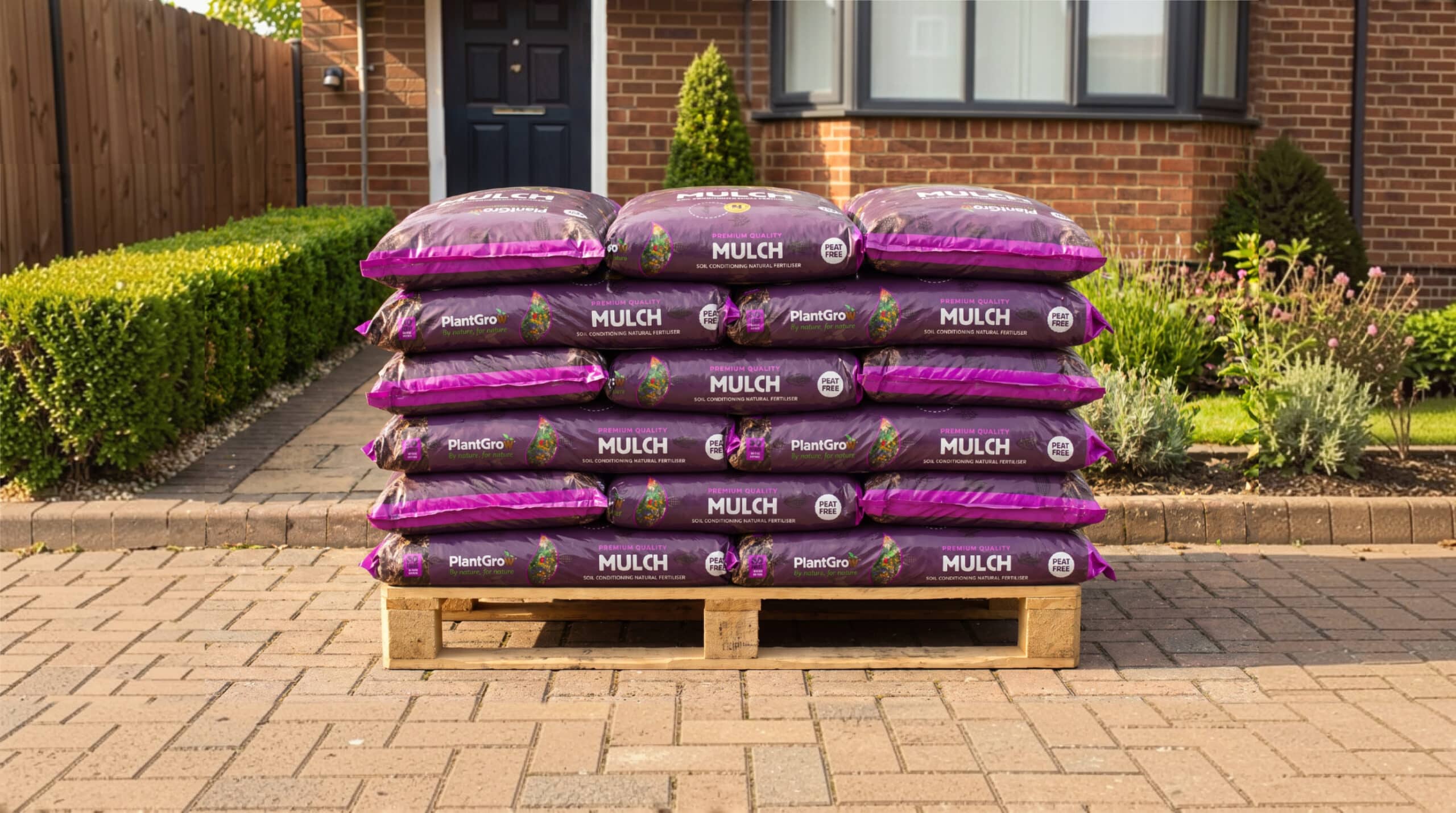 Stacked bags of PlantGrow mulch on wooden pallet in front garden driveway.