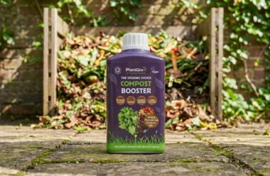 PlantGrow Natural Compost Booster 500ml bottle displayed on paving in a garden setting with compost bin behind.