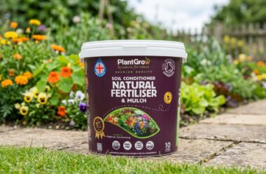 PlantGrow Natural Soil Conditioner 10 litre tub, a plant-based organic soil conditioner and mulch, displayed in a garden setting with flowering plants.