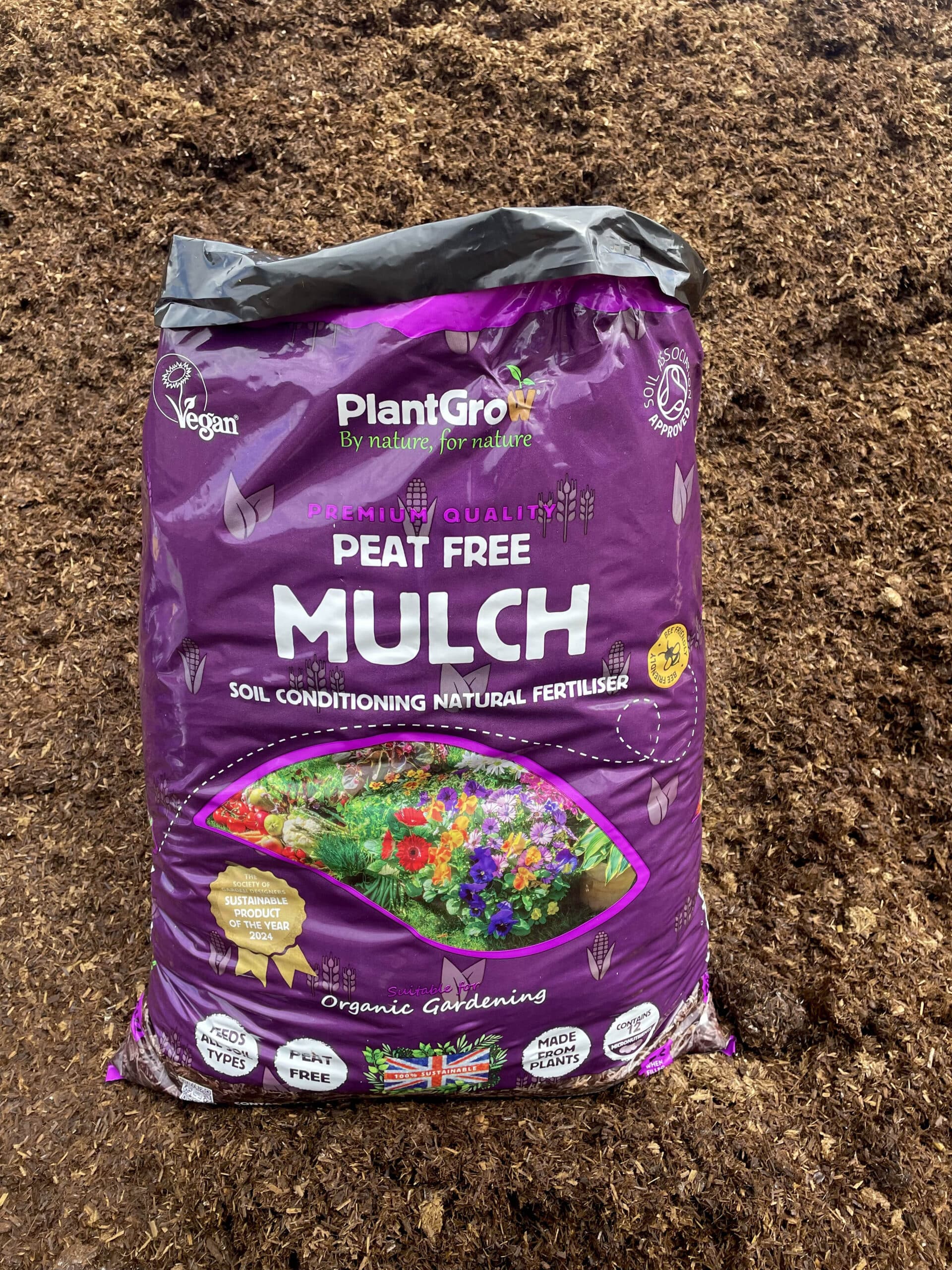 PlantGrow peat-free mulch bag on soil, showing purple packaging with flowering garden imagery and organic gardening certifications.